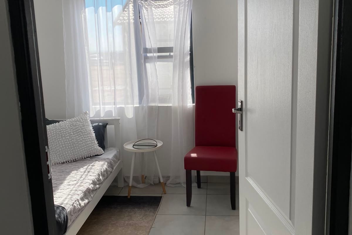A compact bedroom featuring tiled flooring and a white tongue and groove ceiling, viewed through an open doorway.