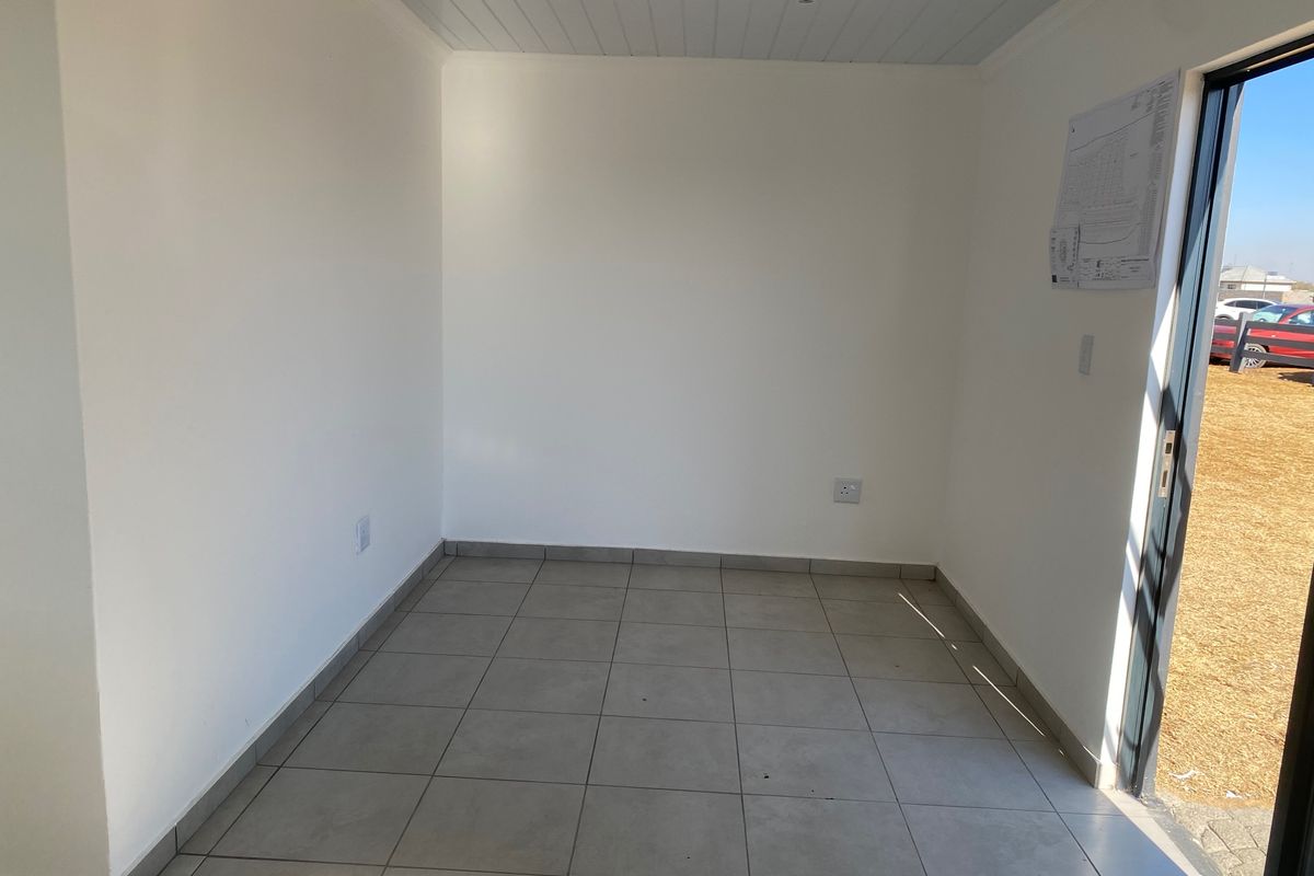 A bright, empty room featuring neutral tiled flooring, a tongue and groove ceiling, and a sliding glass door providing natural light.