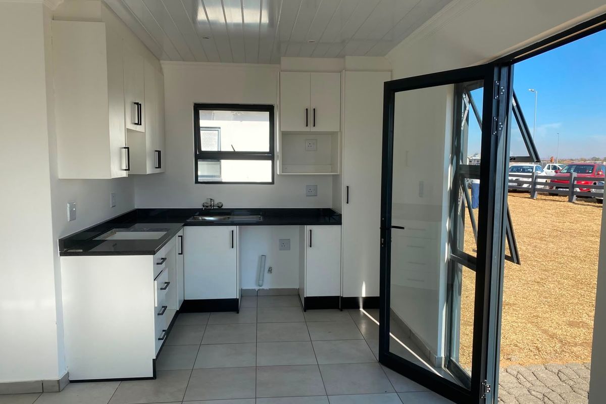 Modern kitchen featuring white cabinetry, dark stone countertops, tiled flooring, and direct access to the exterior through a glass door.