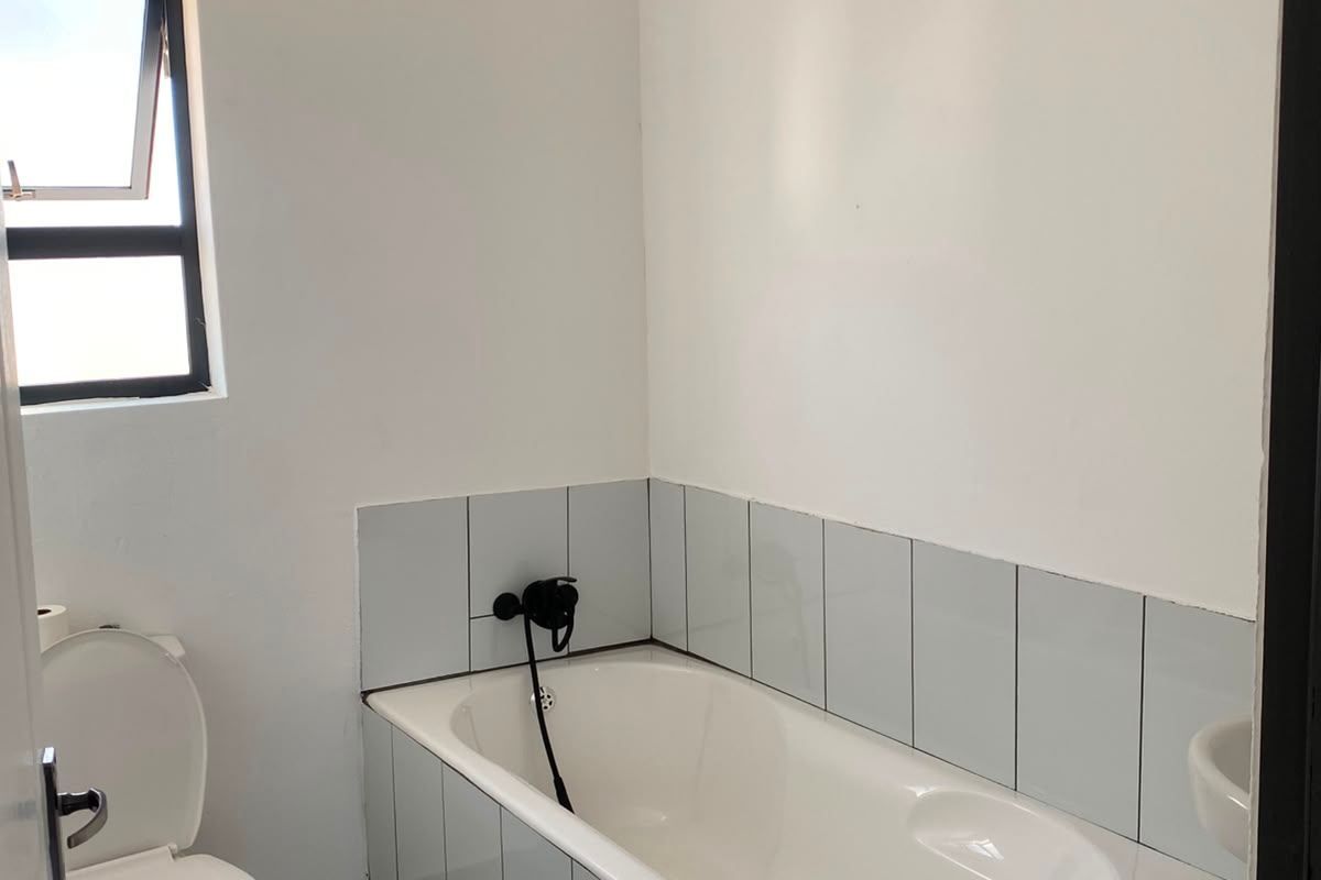 A functional bathroom featuring a bathtub with tiled surround, a standard toilet, and tiled flooring, offering a clean and simple layout.