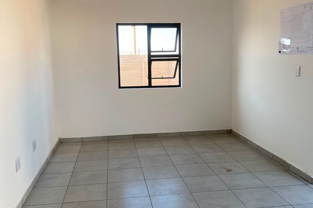 A clean, empty bedroom featuring neutral tiled flooring, white walls, and a modern aluminium window frame, ready for personalization.
