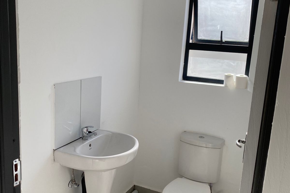 A compact, functional bathroom featuring a pedestal basin, toilet, and tiled flooring, illuminated by a single window.