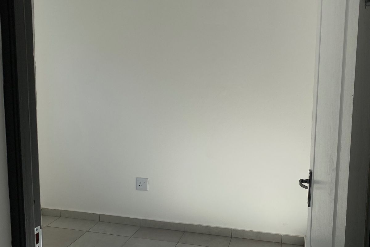 A bright, empty bedroom featuring neutral tiled flooring, a white tongue and groove ceiling with recessed lighting, and a clean, minimalist aesthetic.