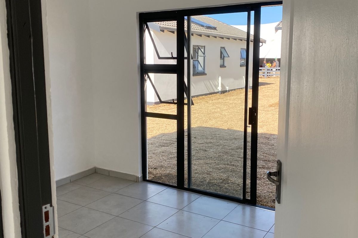 A bright, empty living space featuring modern tiled flooring, a tongue and groove ceiling, and a sliding glass door leading to the rear garden.