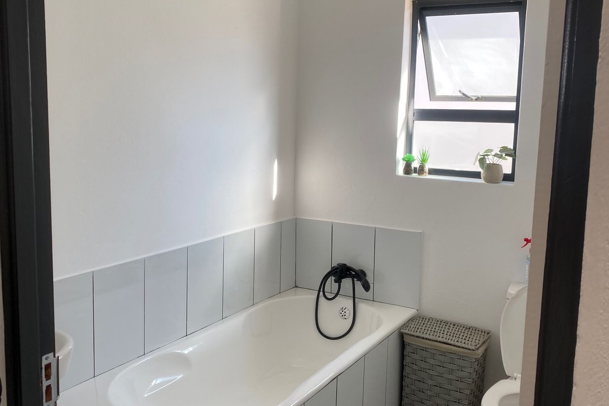 A clean, functional bathroom featuring a built-in bathtub with tiled surround, a toilet, and a top-hung window providing natural light.