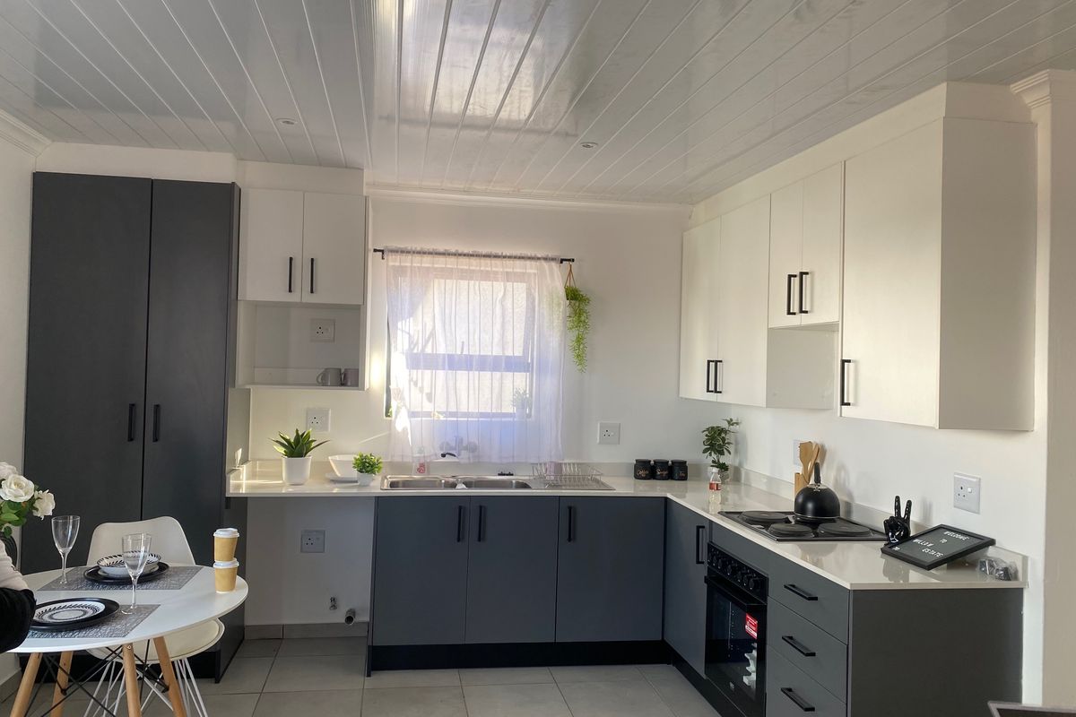 Modern kitchen featuring two-tone cabinetry, built-in oven and hob, double sink, and tiled flooring under a clean tongue and groove ceiling.