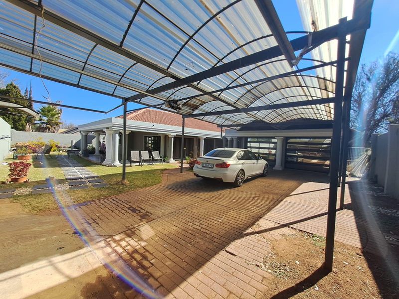Front exterior view featuring a large covered carport, paved driveway, double garage, and a covered patio with architectural columns.