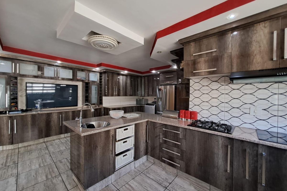 Modern kitchen featuring dark wood-grain cabinetry, granite countertops, gas hob, extractor fan, and tiled flooring with a functional layout.