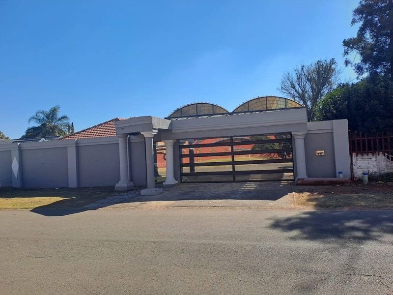 Front view of the property featuring a secure perimeter wall, gated driveway entrance, and decorative pillars with a covered canopy structure.