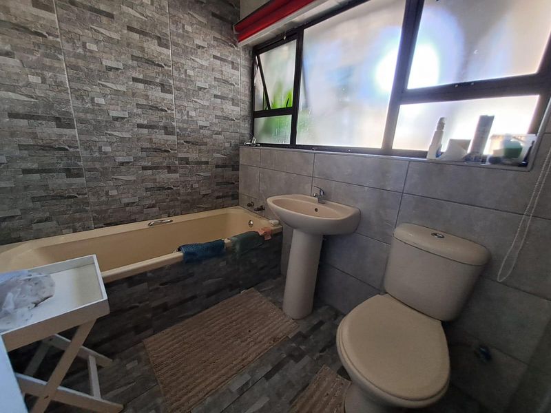 A functional bathroom featuring a pedestal basin, built-in bathtub, and toilet, finished with textured wall tiles and a frosted window for privacy.