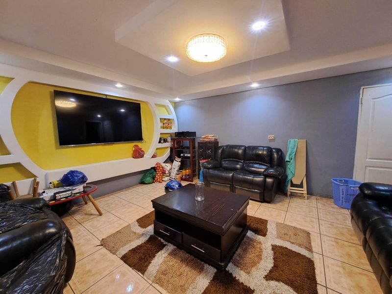 A living room featuring a custom built-in media wall with yellow accent, recessed ceiling lighting, and ceramic tiled flooring.