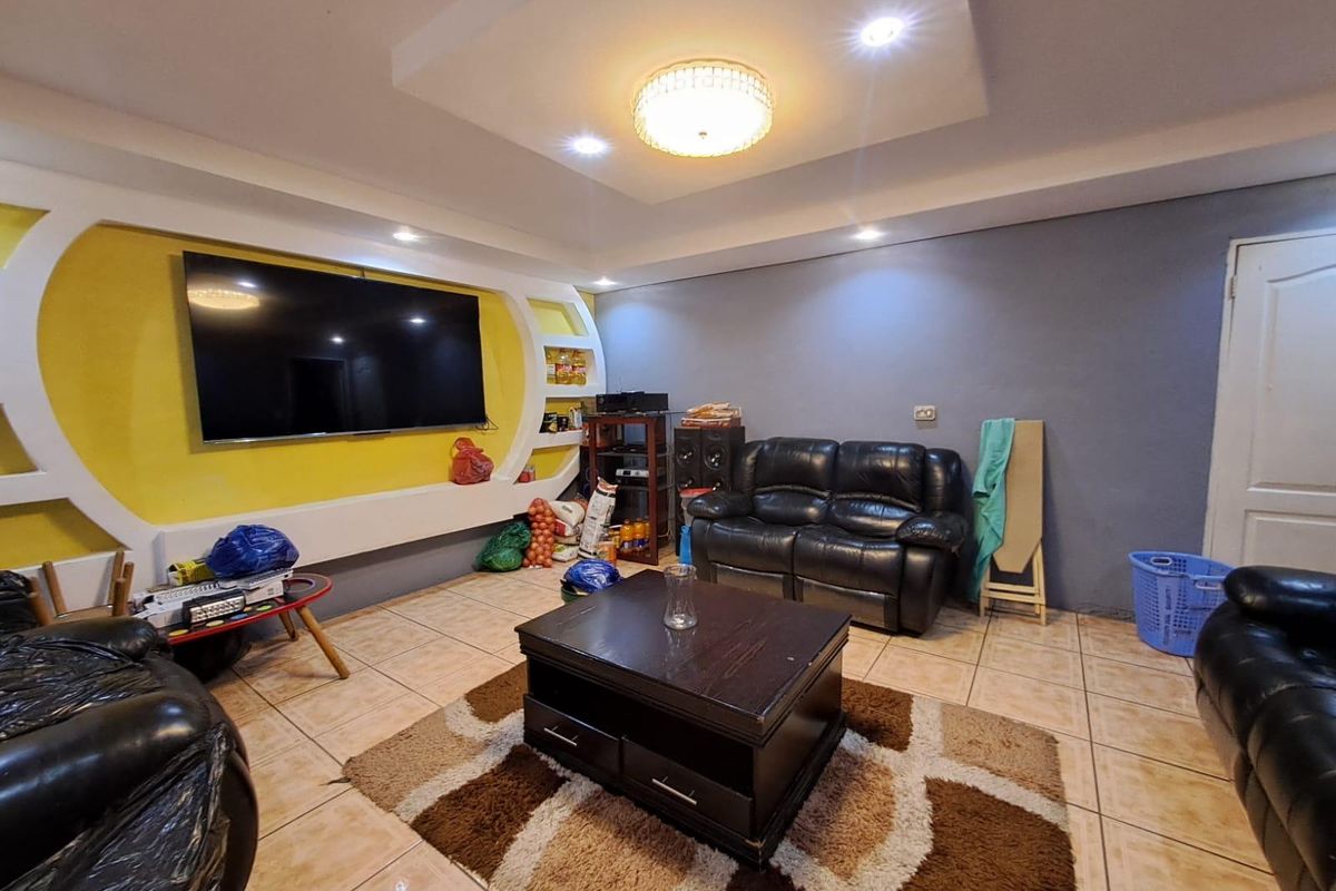 A living room featuring a custom built-in media wall with yellow accent, recessed ceiling lighting, and ceramic tiled flooring.
