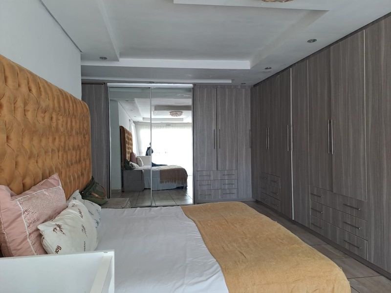 Spacious bedroom featuring extensive built-in cabinetry with mirrored doors, recessed ceiling lighting, and neutral tiled flooring.