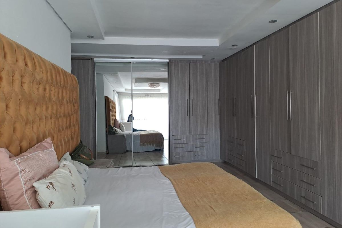 Spacious bedroom featuring extensive built-in cabinetry with mirrored doors, recessed ceiling lighting, and neutral tiled flooring.