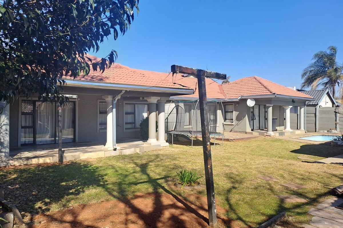 Rear view of the house featuring a covered patio, tiled roof, and a swimming pool set within a spacious garden area.