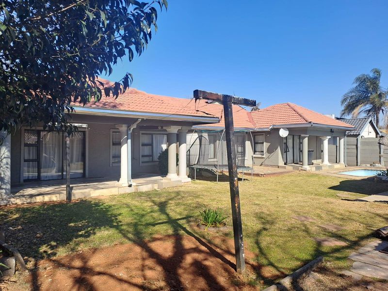 Rear view of the house featuring a covered patio, tiled roof, and a swimming pool set within a spacious garden area.