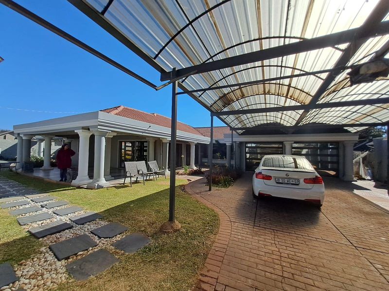 Front exterior view featuring a paved driveway, a large covered carport, and a spacious covered patio with classic columns.