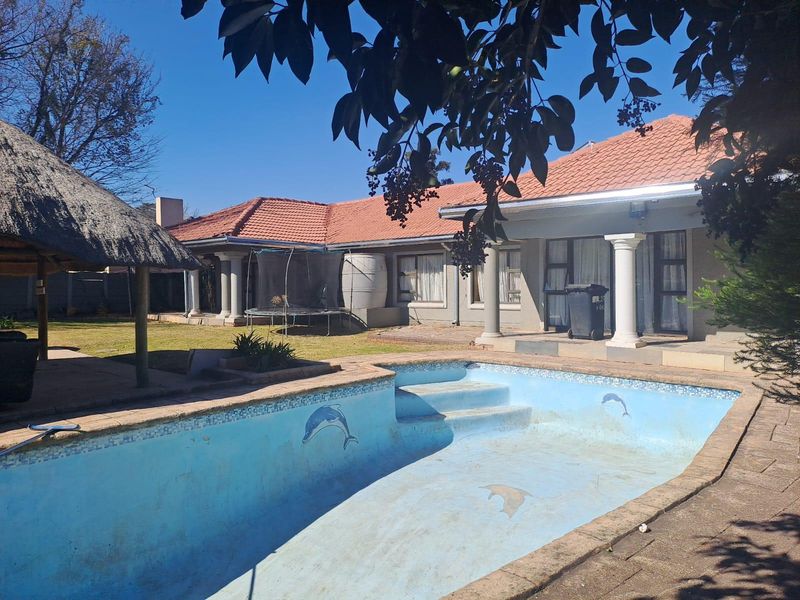 Rear exterior view featuring a swimming pool, a thatched lapa, and a covered patio area attached to the main house structure.
