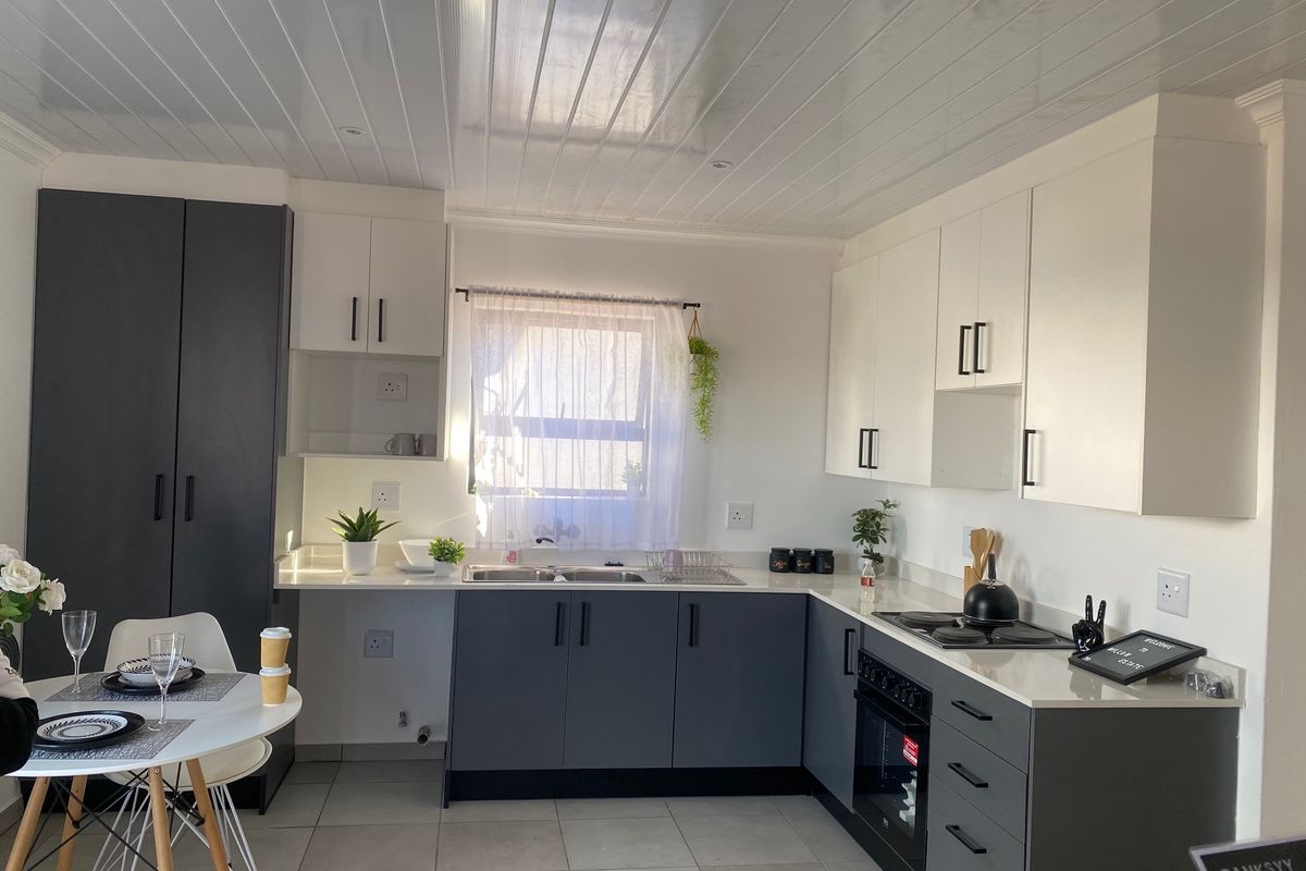 Modern kitchen featuring two-tone cabinetry, stone countertops, built-in oven and hob, and a clean tiled finish with a bright, functional layout.