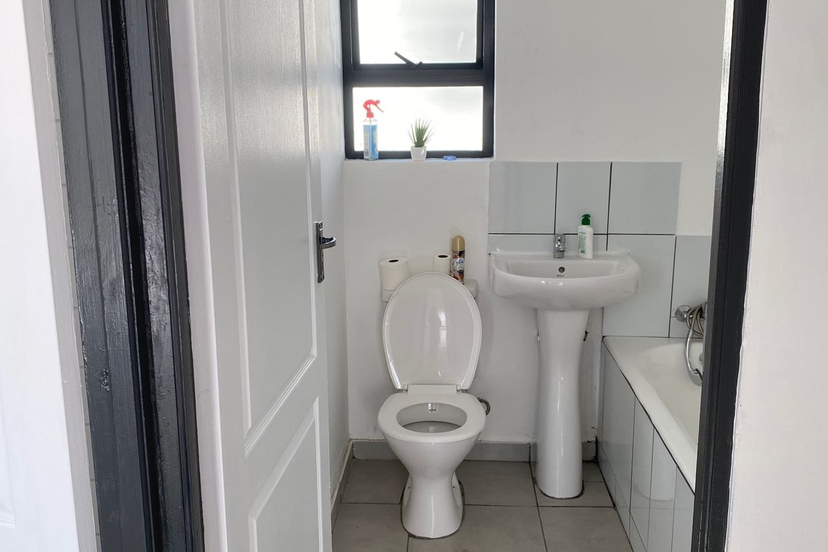 A functional bathroom featuring a pedestal basin, toilet, and bathtub with tiled flooring and splashbacks, illuminated by a window.
