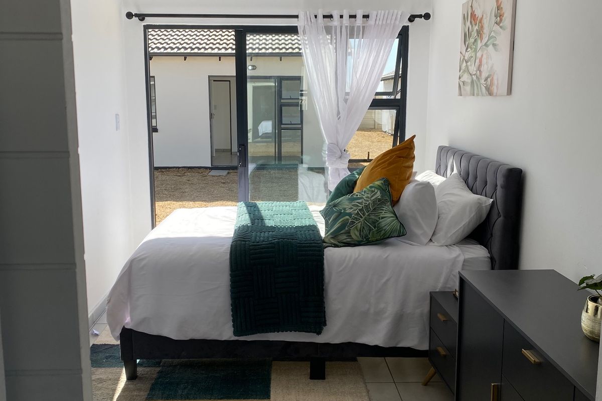 A bright bedroom featuring tiled flooring, a tongue and groove ceiling, and a large sliding glass door providing direct access to the rear exterior.