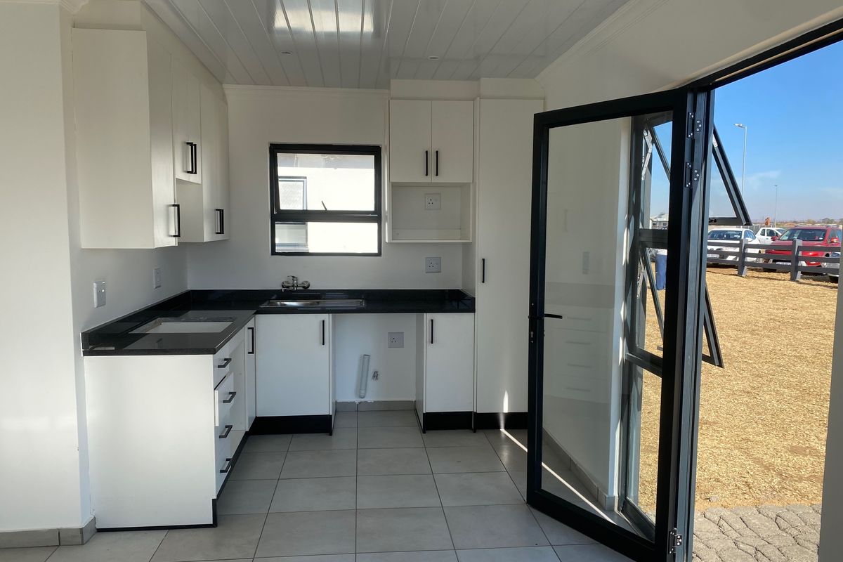 Modern kitchen featuring white cabinetry, contrasting black countertops, tiled flooring, and direct access to the exterior through a glass door.