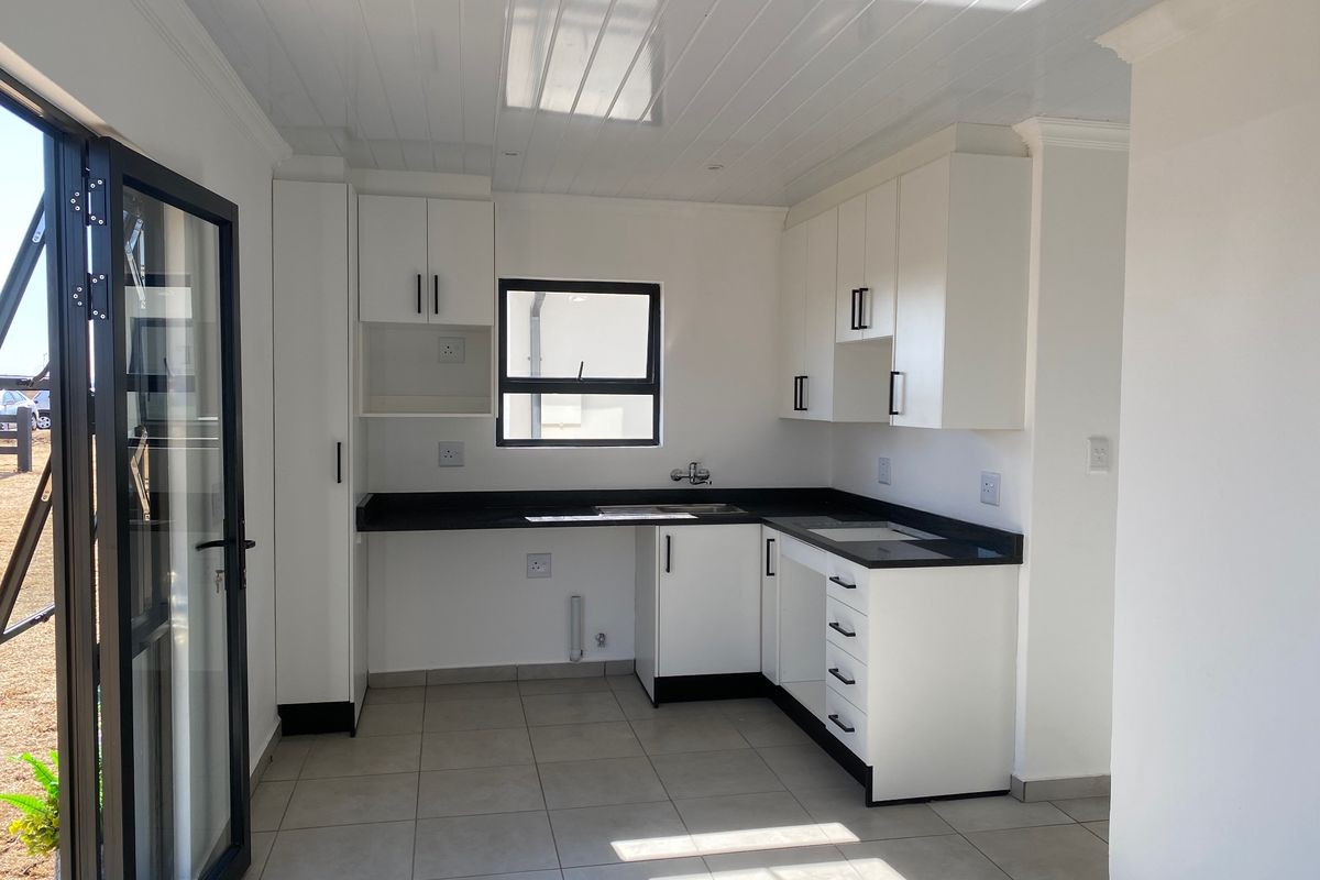 A modern, clean-lined kitchen featuring white cabinetry, contrasting dark countertops, tiled flooring, and a bright tongue and groove ceiling with direct outdoor access.