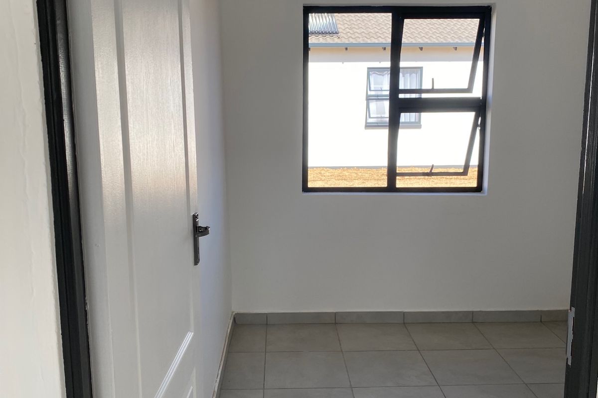 A clean, empty bedroom featuring neutral tiled flooring, white walls, and a modern aluminium window frame, offering a blank canvas for personalization.