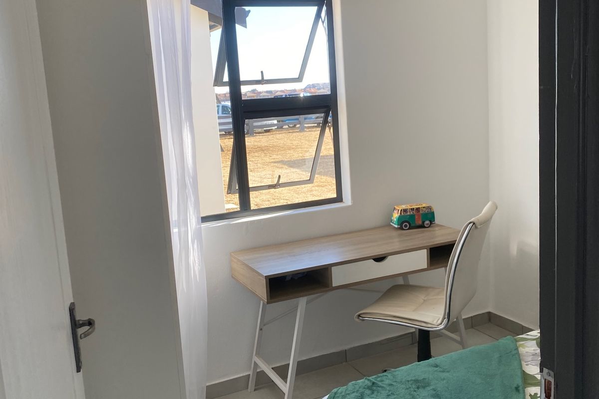A compact bedroom featuring tiled flooring, a modern aluminium window frame, and a clean white tongue and groove ceiling.