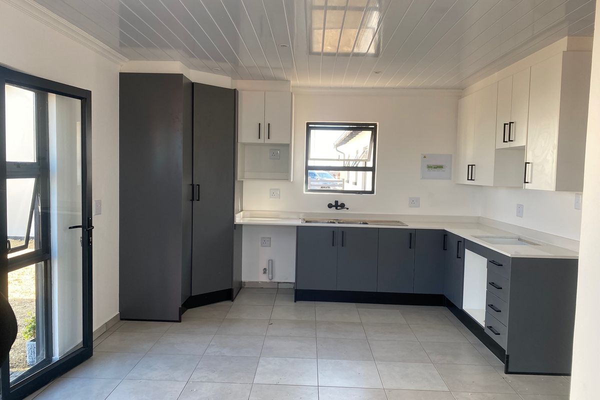 Modern, empty kitchen featuring two-tone cabinetry, stone countertops, double sink, and tiled flooring with direct access to the exterior.