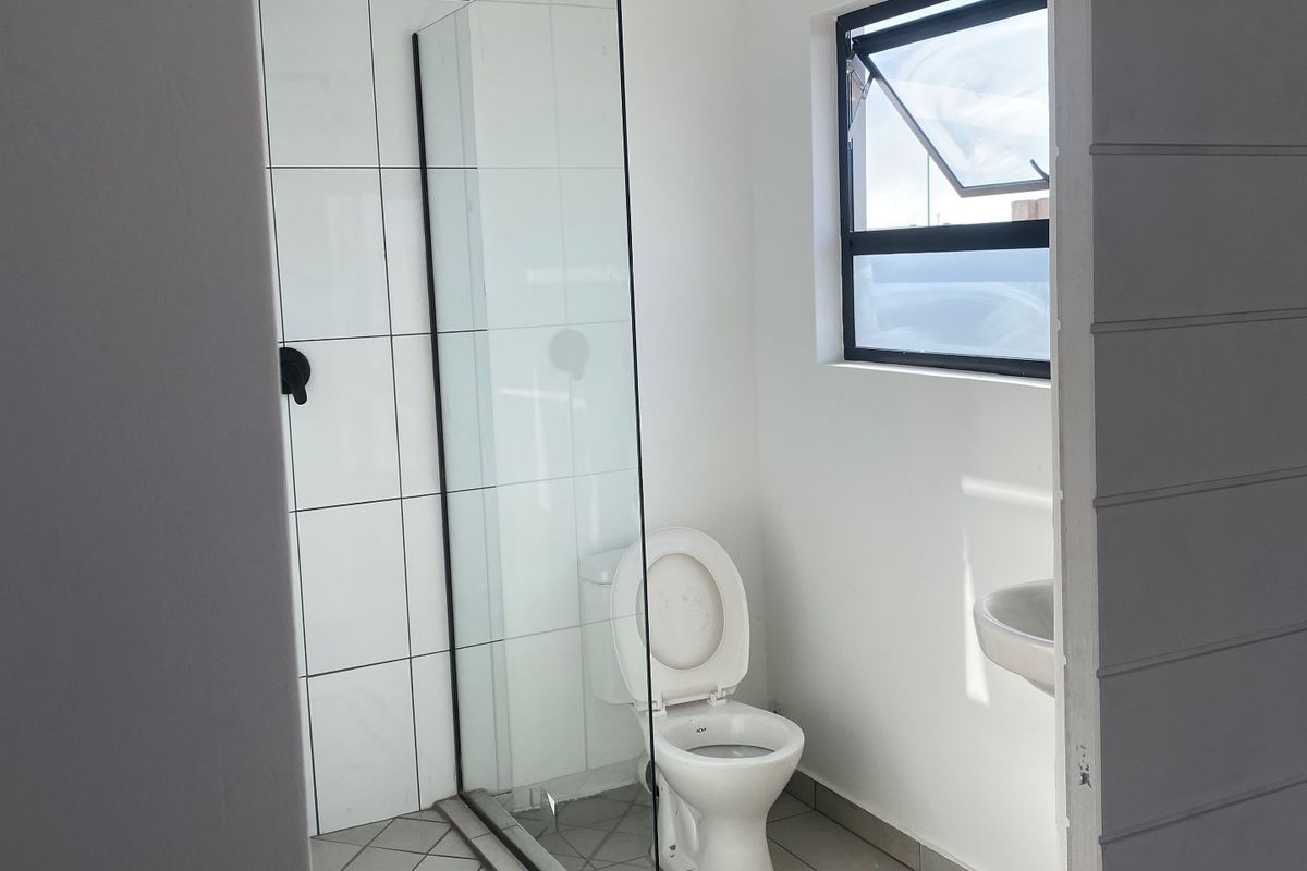 A clean, modern bathroom featuring a glass-enclosed shower, tiled flooring, and a wall-mounted toilet with a bright, neutral aesthetic.