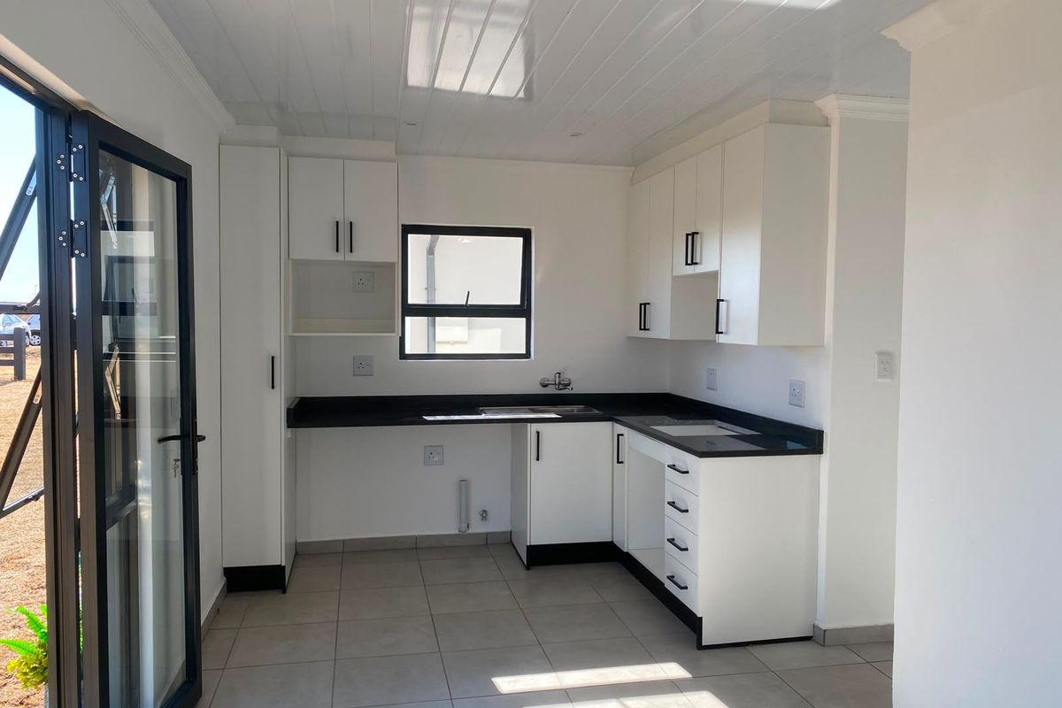 A clean, modern kitchen featuring white cabinetry, contrasting black countertops, tiled flooring, and a bright tongue and groove ceiling with direct outdoor access.