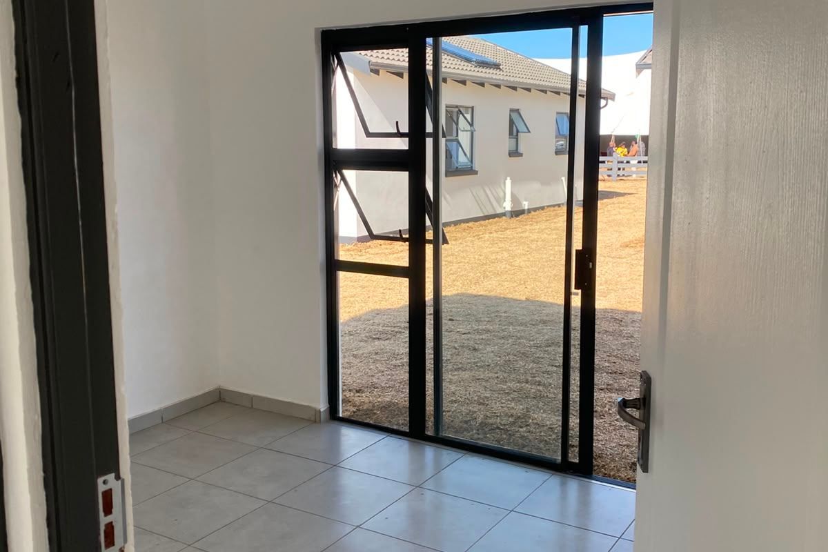 A bright, empty living space featuring neutral tiled flooring, recessed ceiling lights, and a sliding glass door providing direct access to the rear yard.