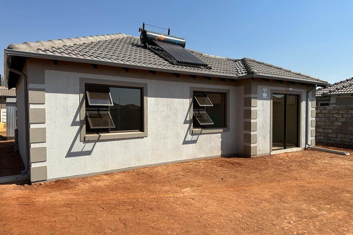 Rear view of a modern single-story house featuring a tiled roof, solar water heating system, and aluminium window frames with an unlandscaped yard.