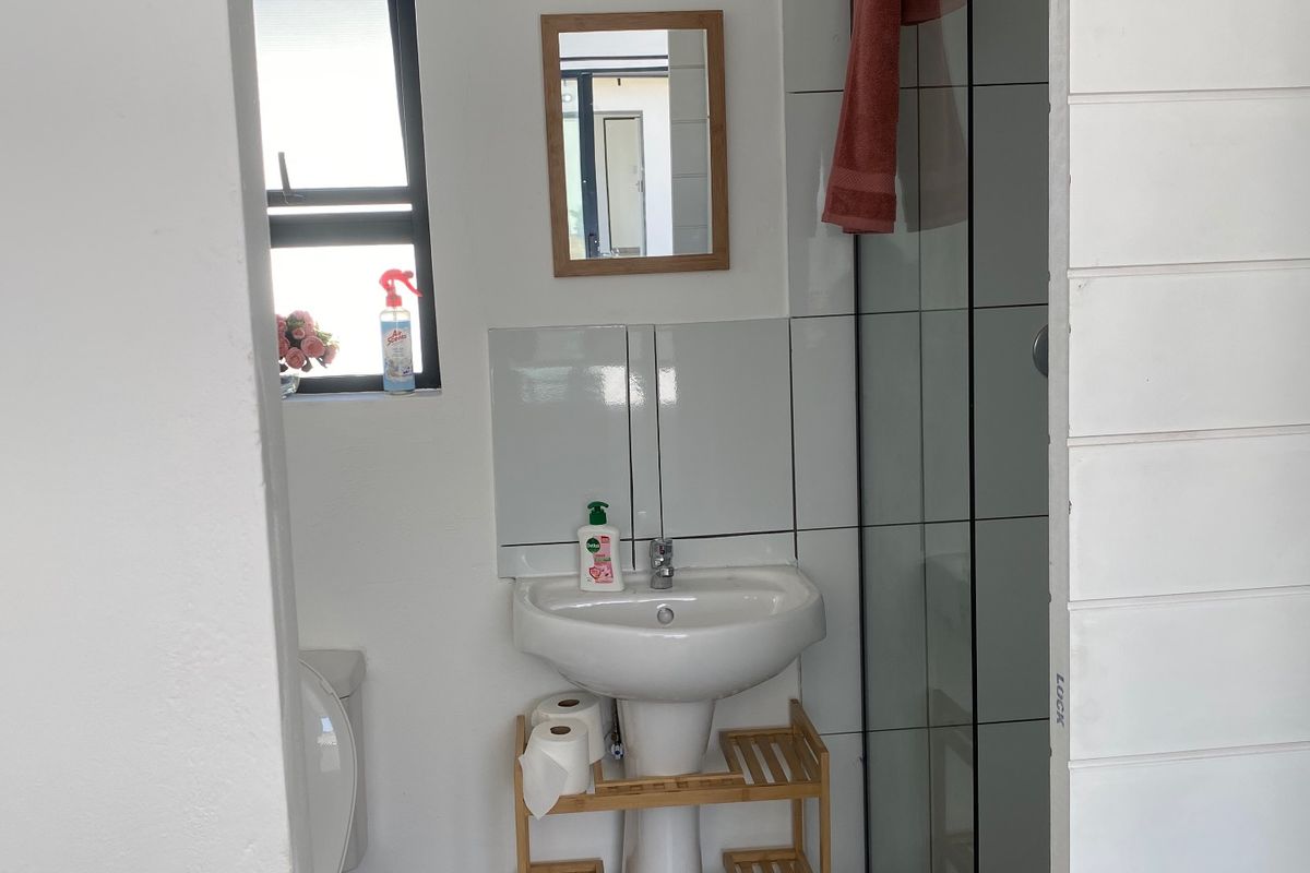 A functional bathroom featuring a pedestal basin, tiled splashback, and a glass-enclosed shower with neutral floor tiling.