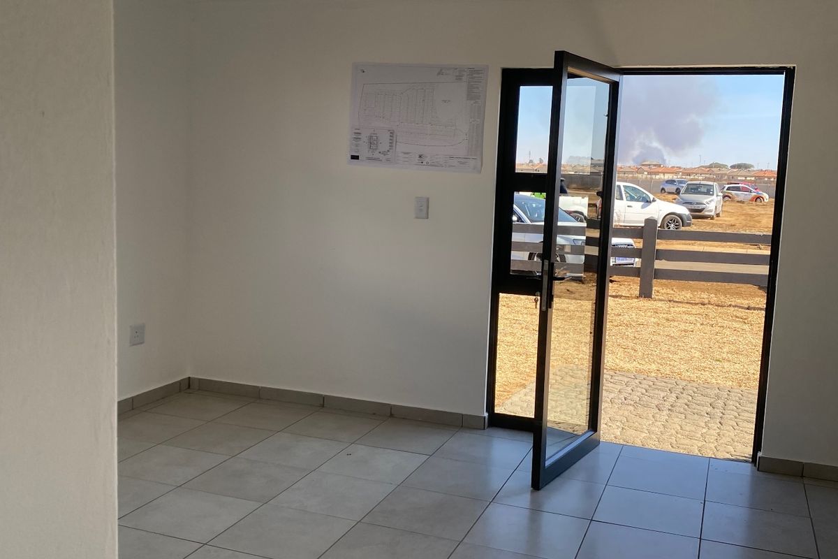 A bright, empty living space featuring neutral tiled flooring, a white tongue and groove ceiling, and a modern glass door leading to the exterior.