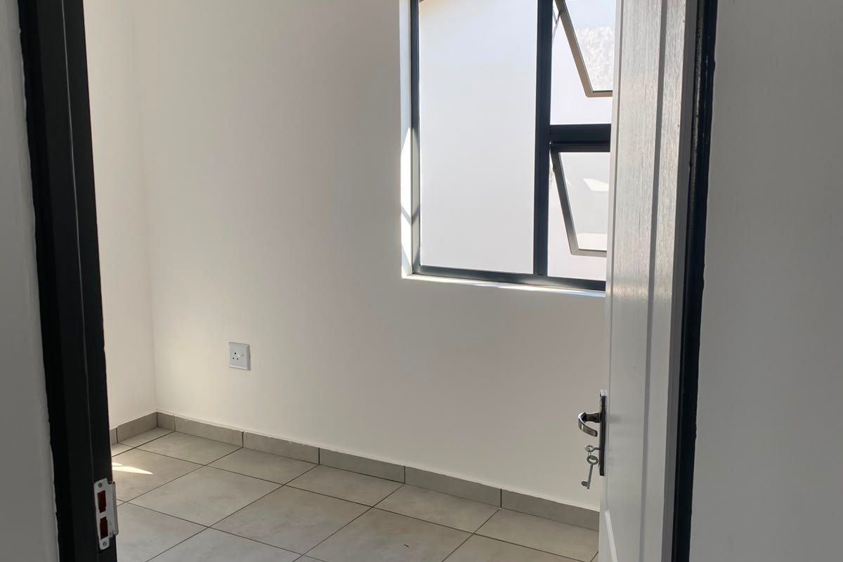 A clean, empty bedroom featuring neutral tiled flooring, a white tongue and groove ceiling, and a modern aluminium window frame.