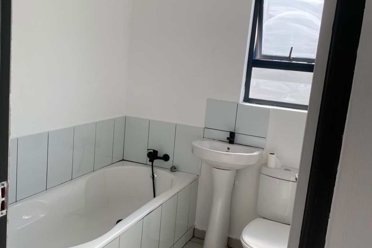 A clean, functional bathroom featuring a white bathtub, pedestal basin, toilet, and neutral tiled finishes, offering a simple and practical layout.