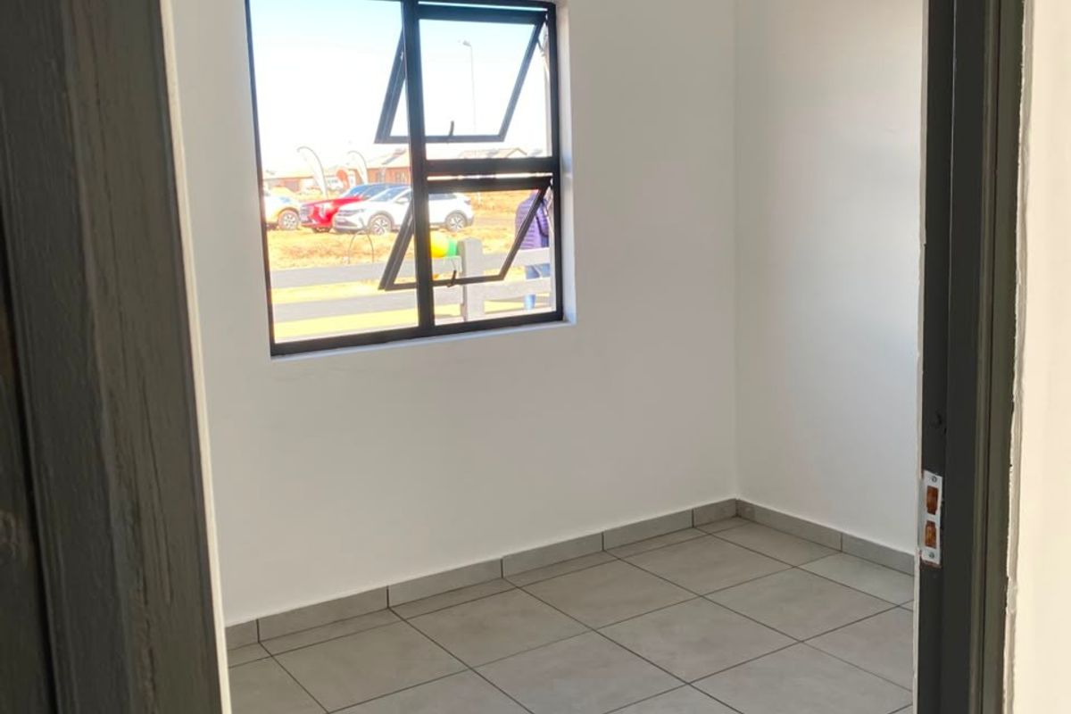 A clean, empty bedroom featuring neutral tiled flooring, white walls, and a modern aluminium window frame.