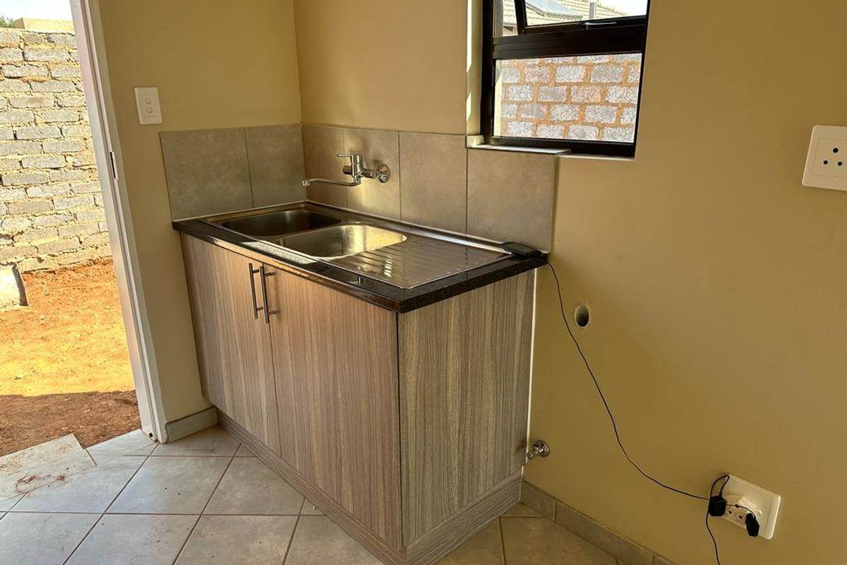 A compact kitchen area featuring a stainless steel sink, laminate cabinetry, tiled splashback, and tiled flooring with direct access to the exterior.