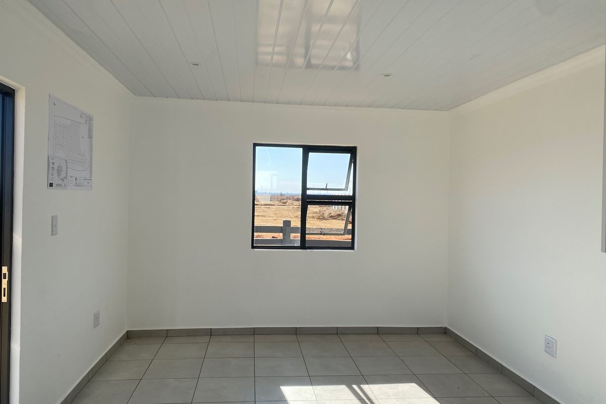 A bright, empty living area featuring neutral tiled flooring, a modern tongue and groove ceiling, and a large window providing natural light.