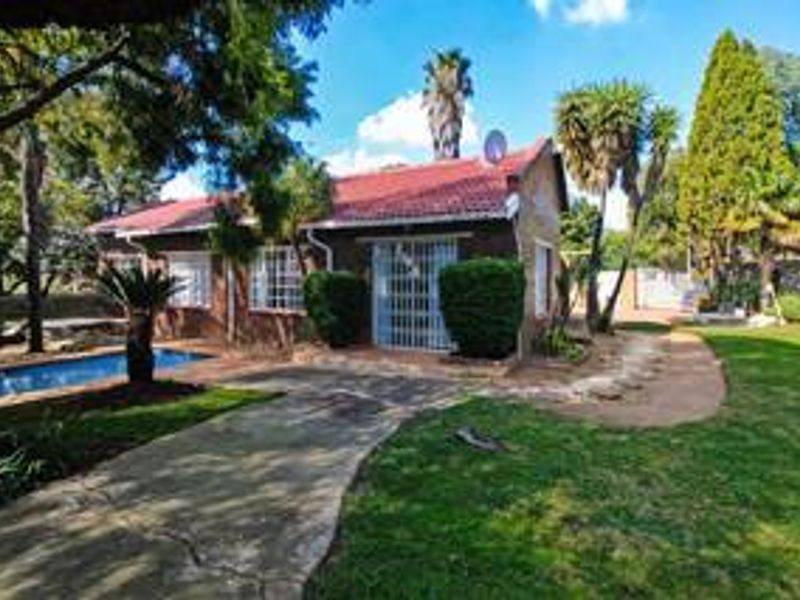 Rear view of the property featuring a swimming pool, paved walkway, and established garden area with a tiled roof structure.