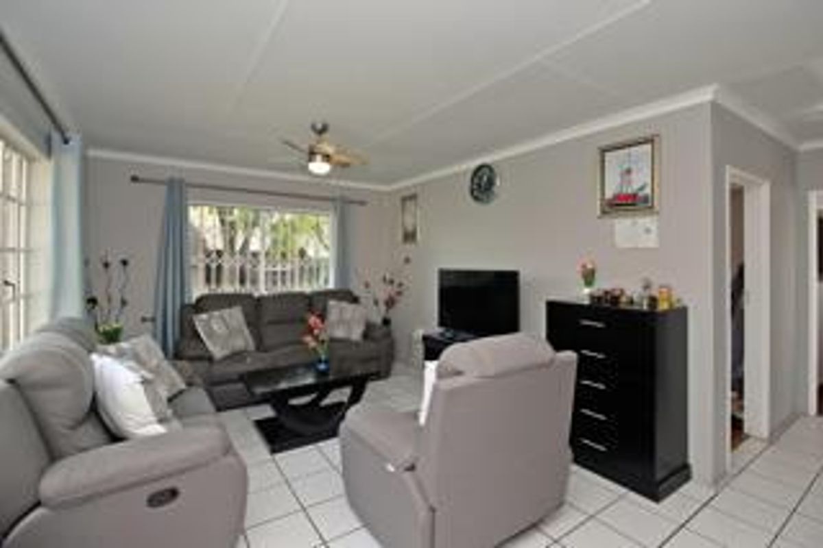 A comfortable living room featuring tiled flooring, a ceiling fan, and large windows with security gates, providing a functional and well-lit space.