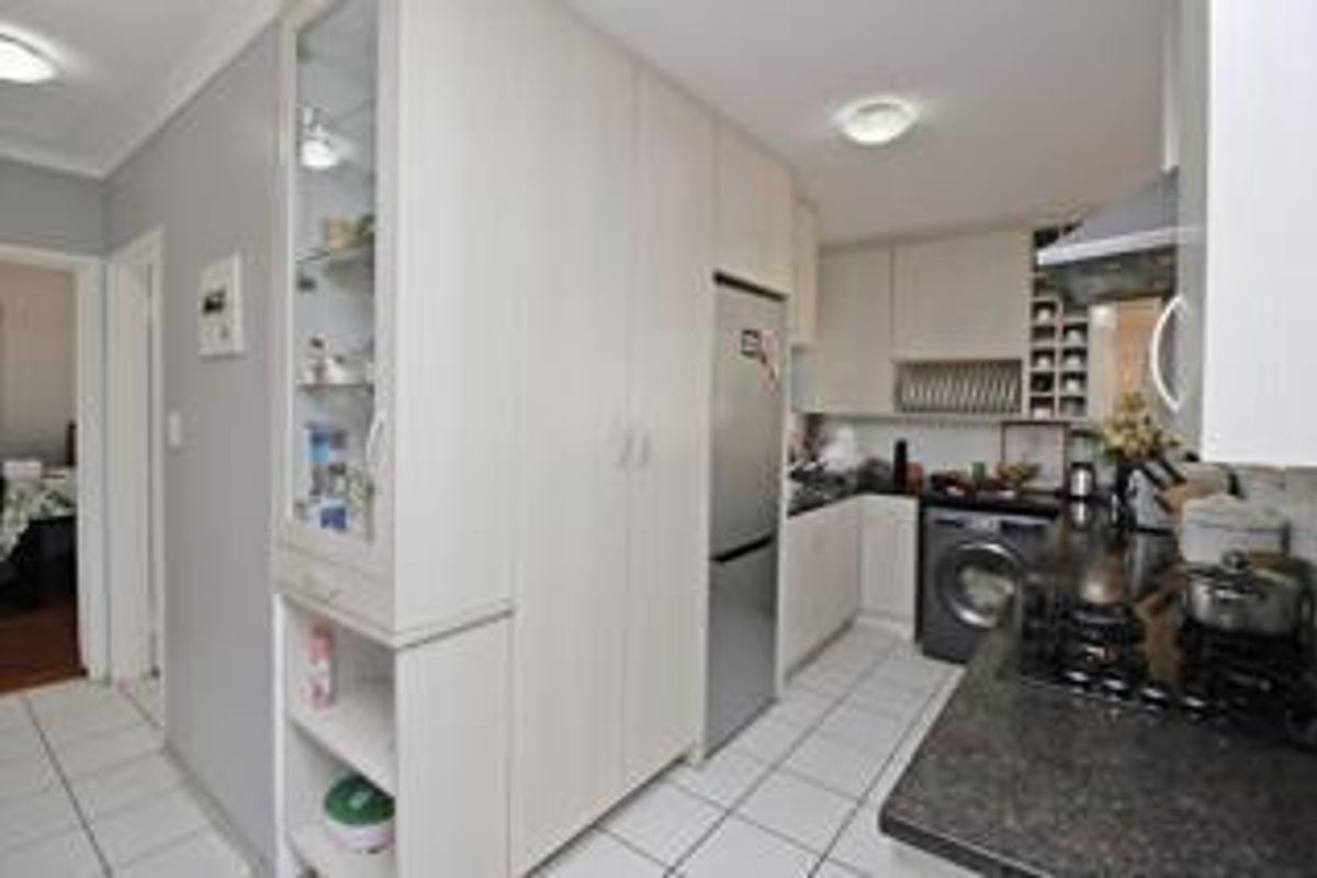 Compact kitchen featuring light-toned cabinetry, dark granite countertops, a gas hob with extractor, and integrated laundry appliances with tiled flooring.