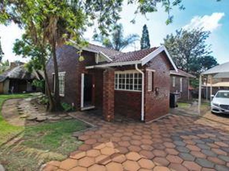 A brick-faced house exterior featuring a tiled roof, paved driveway, and a carport, set within a landscaped garden area.