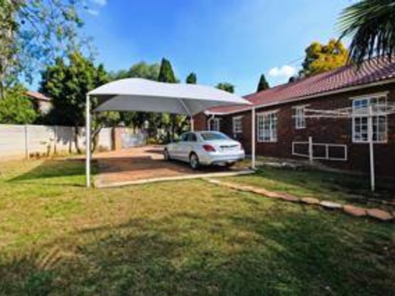 Rear exterior view of the property featuring a brick facade, tiled roof, paved driveway with a shade sail, and a spacious lawn.