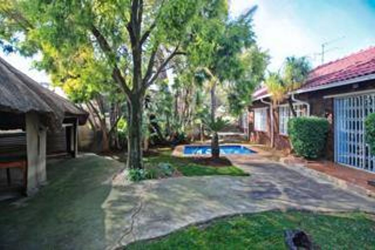 Rear garden area featuring a swimming pool, paved patio space, and a traditional thatched lapa structure.