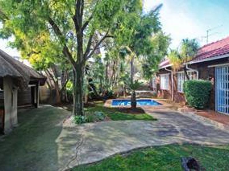 Rear garden area featuring a swimming pool, paved patio space, and a traditional thatched lapa structure.