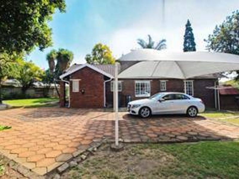 Front exterior view of a brick house featuring a paved driveway and a large shade sail structure.