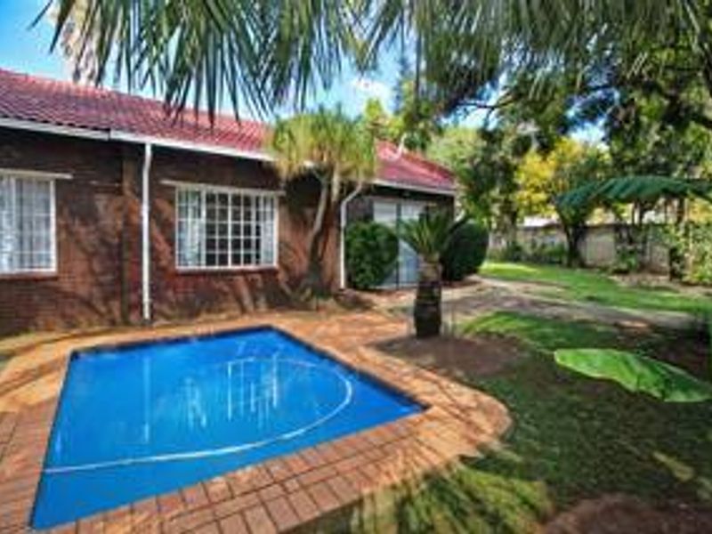 Rear exterior view featuring a swimming pool with brick paving, established garden, and a brick-faced house with a tiled roof.
